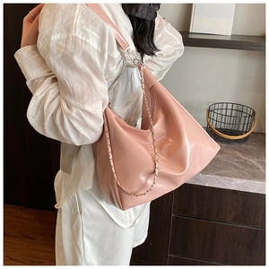 Close-up of pink glossy pleated hobo bag with a decorative metal chain strap on a model
