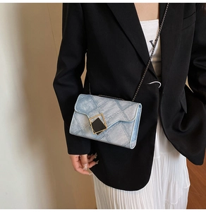 Detail of light blue denim crossbody bag with quilted texture and gold metal buckle
