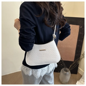 Detail shot of white woven shoulder bag with golden metal bar and knotted strap