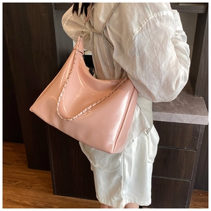 Close-up of bright pink pleated hobo bag with glossy leather finish and metal chain