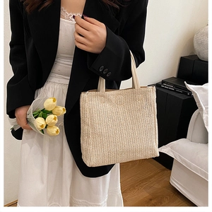 Detail of hand-woven beige straw tote bag styled with yellow tulips and minimalist chic outfit