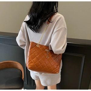 Detailed view of quilted caramel leather tote bag with gold chain strap on model