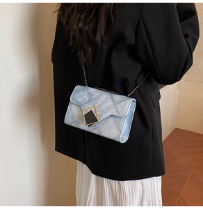 Close-up of light blue denim texture crossbody bag with gold-trimmed black heart buckle