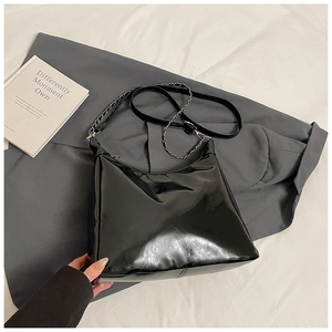 Detail of glossy black tote bag featuring metallic chain strap and minimalist finish