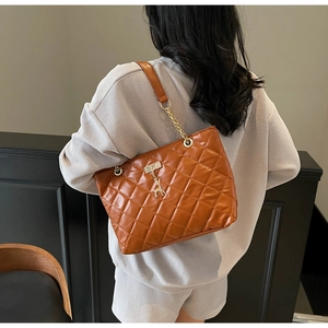 Detail of brown quilted tote bag with gold chain strap and deer pendant on model