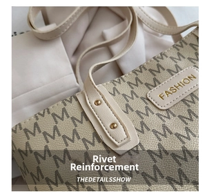 Close-up of beige tote bag with M-pattern, gold rivets, and a Fashion label detail