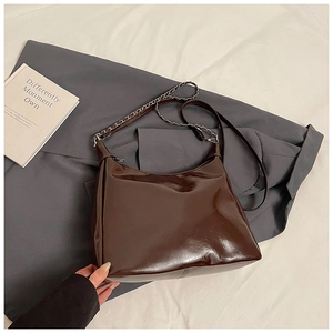 Detail of dark brown patent leather hobo bag with metal chain strap on gray suit blazer