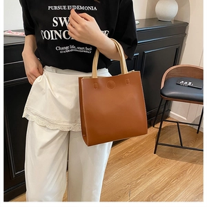 Detail of brown faux leather tote bag with beige handles and decorative stitching patterns