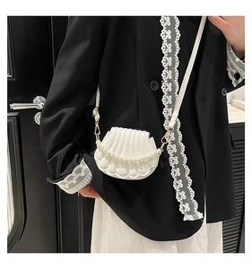 Détail du sac blanc en forme de coquille avec texture plissée et poignée en perles