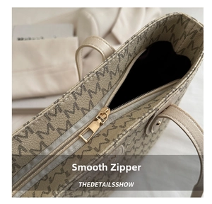 Close-up of the smooth metal zipper and monogram pattern on the beige tote bag