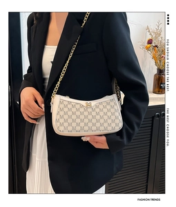 Detail of white baguette bag with gold M-buckle, chain strap, and monogram pattern