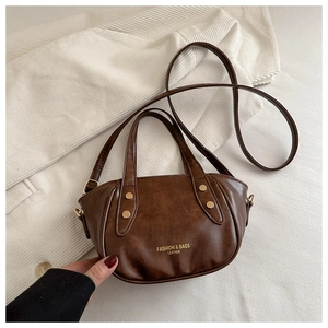Détail du sac à main en cuir marron avec clous dorés sur fond de tissu blanc texturé