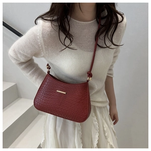 Detail of burgundy crocodile pattern shoulder bag with gold metal buckle and knotted strap