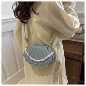 Sac bandoulière bleu forme coquillage avec anse en perles porté par un mannequin chic