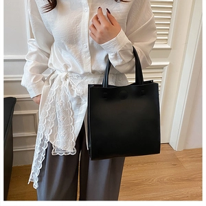 Minimalist black matte leather tote bag with round magnetic clasp held by a female model