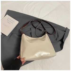 Detail of cream tote bag featuring brown leather strap and silver chain accents