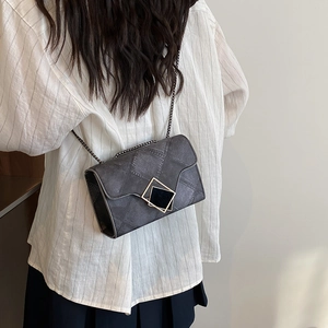 Chic dark gray quilted chain crossbody bag with geometric gold clasp worn on person