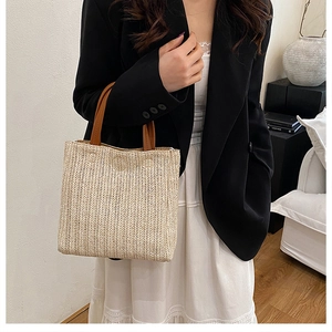 Close-up of beige woven straw tote bag with brown leather handles on a model