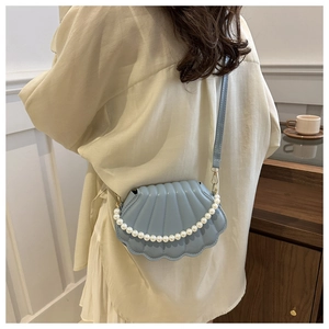 Sac bandoulière coquillage bleu clair avec chaîne perlée et texture matelassée sur modèle