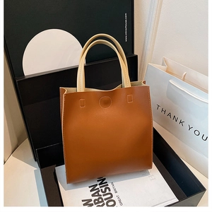 Detail of a brown leather tote bag with beige handles displayed on stylish urban books