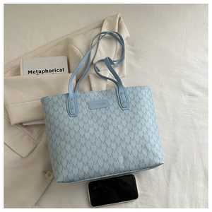 Flat lay detail of a light blue monogram tote bag with a metal Fashion label and book