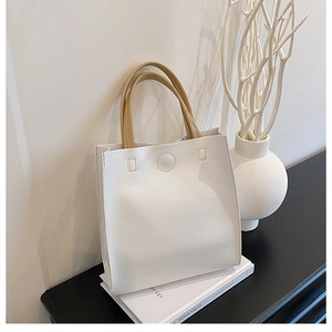 Minimalist cream white PU leather tote bag with brown straps in a lifestyle setting