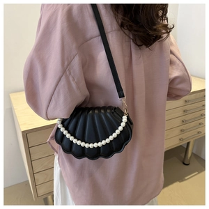 Détail d'un sac bandoulière noir en forme de coquille avec poignée élégante en perles