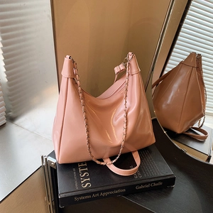 Pink glossy leather tote bag with chain strap displayed on a book for a modern look