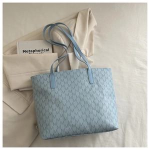 Detail of light blue leather tote bag with repetitive M letter pattern on soft fabric
