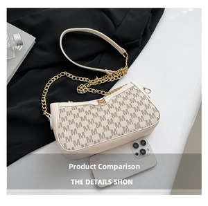Detail view of cream shoulder bag with M-pattern print and gold chain next to a phone