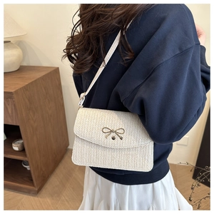 Detail of woven beige texture and gold bow buckle on a stylish crossbody bag