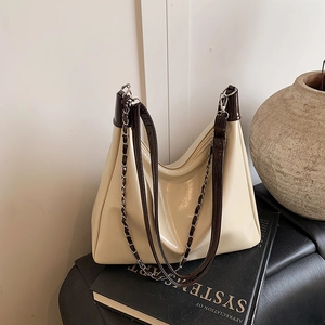 Large cream pleated tote bag with brown trim and metal chain on a black book
