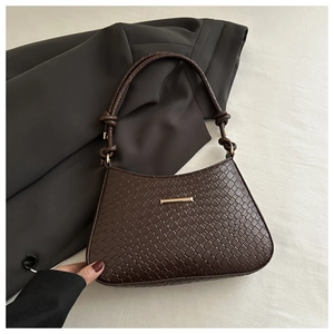 Detail of dark brown woven underarm bag with knotted strap and gold metal hardware accent