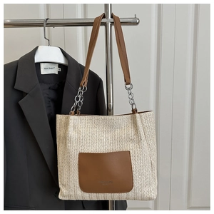 Detail of woven straw tote bag with brown leather pocket and silver chain strap