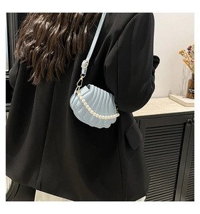 Détail d'un sac bandoulière bleu clair en forme de coquille avec une chaîne de perles