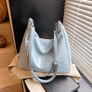 Light blue pleated tote bag with silver chain strap on a vintage book and trench coat