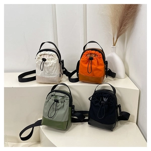 Nylon drawstring crossbody bags in cream, orange, green, and black on a tiered stand
