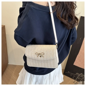 Close-up of cream straw crossbody bag with golden bow clasp on a model's shoulder