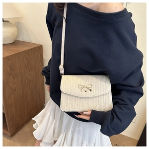 Close-up of a cream woven crossbody bag with a golden bow buckle and fine leather strap