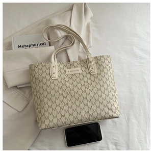 Macro shot of cream tote bag with M-pattern print and slim handles on beige fabric