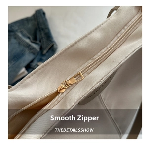 Detail of smooth metal zipper and embossed leather label on solid canvas tote bag
