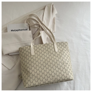 Detailed view of beige large tote bag with classic M-monogram pattern on white fabric