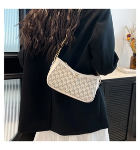 Detail view of white underarm bag with M-pattern texture and gold chain strap worn by model
