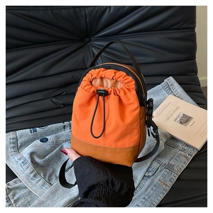 Detail of orange nylon and brown leather mini bucket bag on denim jacket