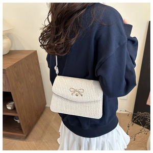 Détail du sac bandoulière en paille tressée avec nœud doré et fine bandoulière blanche