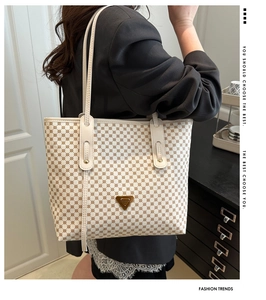 Détail du sac cabas en cuir blanc avec imprimé logo marron et emblème doré brillant
