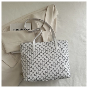 Flat lay of white tote bag with black M-letter monogram and shoulder straps on a blazer