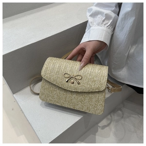 Dettaglio borsa a tracolla in paglia intrecciata beige con fiocco in metallo su scale