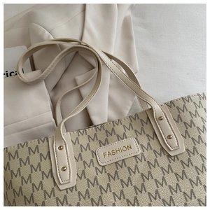 Close-up of cream tote bag featuring letter print, gold logo plate, and stud details