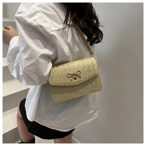 Close-up of beige woven straw shoulder bag with elegant metal bow clasp detail
